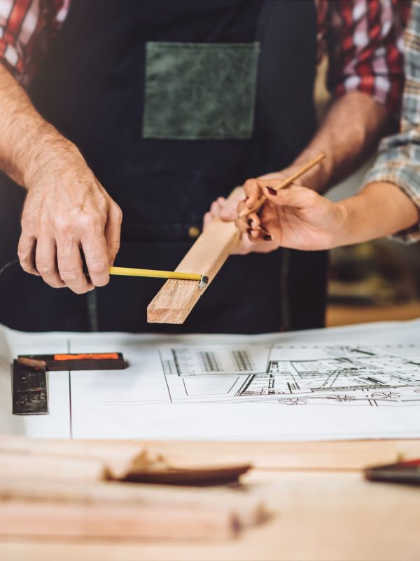 Small business furniture owner and professional architect interior designer working together in carpenter workshop with blueprint and tablet discussing about home furnishing design project.